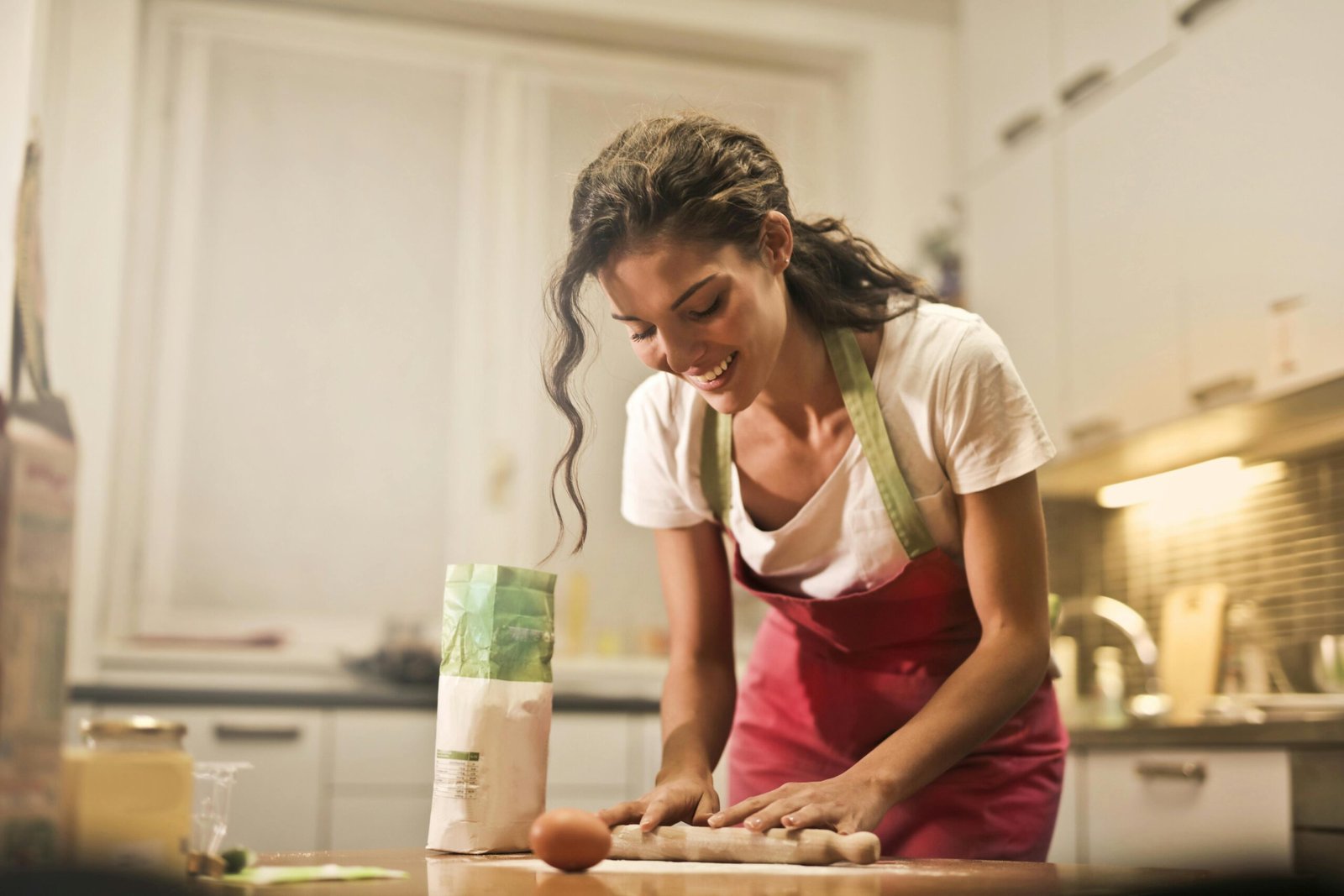 Smiling woman making dough at home, enjoying the baking process.