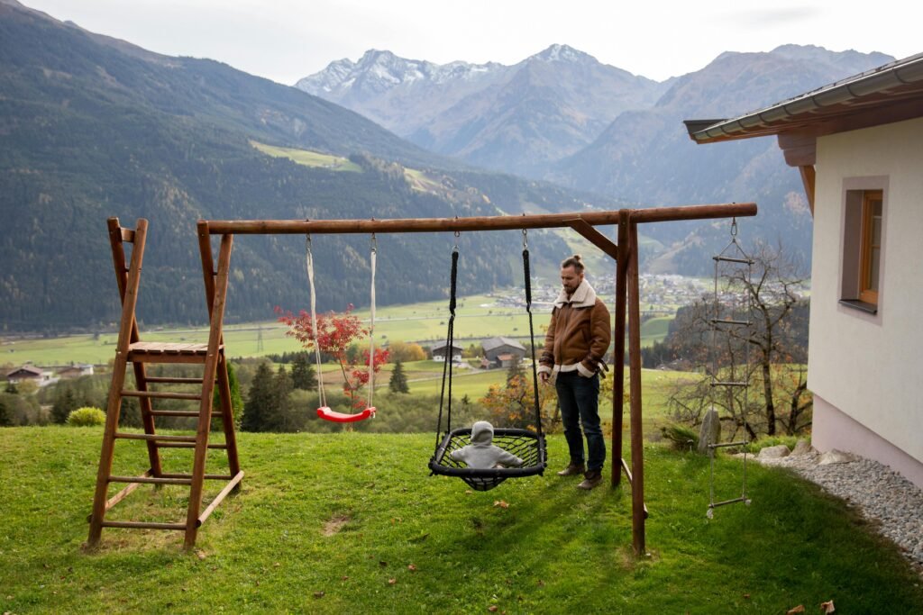 A father and toddler enjoy togetherness on a swing in a scenic mountain landscape.