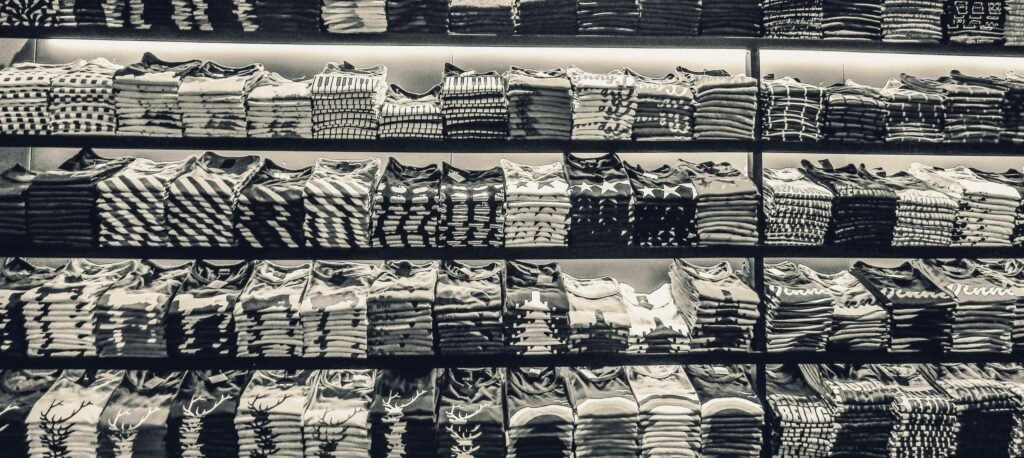 Black and white image showcasing neatly folded t-shirts stacked on store shelves.